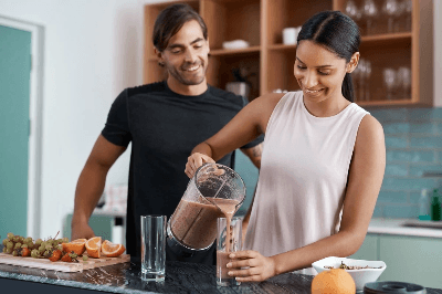 Two people in a kitchen prepare a fresh fruit smoothie, highlighting healthy nutrition and wellness with vibrant fruits on the counter.