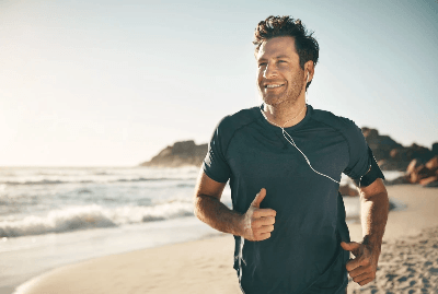 Almased person jogging along sandy beach with ocean waves, highlighting fitness, energy and healthy lifestyle in natural outdoor setting