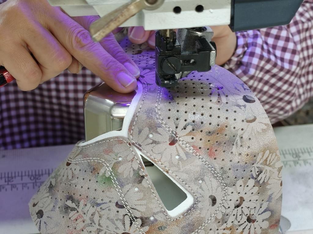 A skilled craftsman's hands guide genuine leather under the sewing machine needle, demonstrating precise control in women's shoe upper stitching.