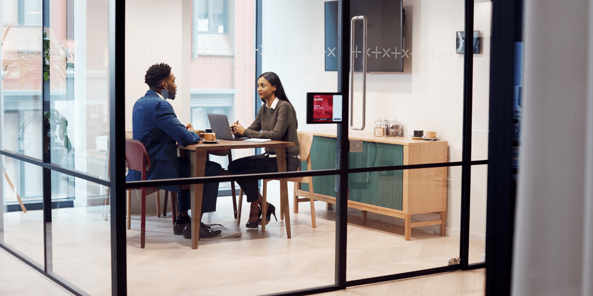 Un homme et une femme assis l’un en face de l’autre, discutant lors d'une session de formation média personnalisée, axée sur la pratique d'entrevue.