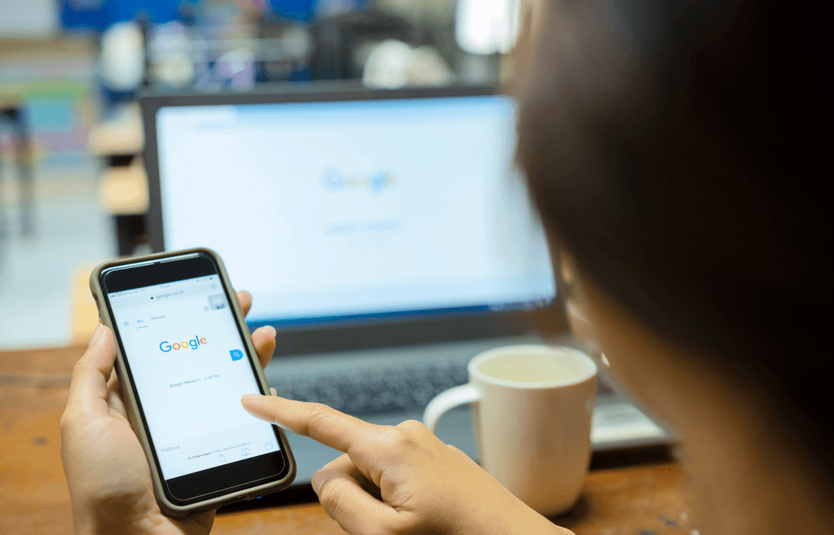 A person holding a smartphone while performing a search on Google’s mobile version.