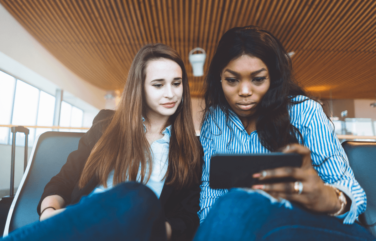 Two women sit side by side watching video content on a smartphone.
