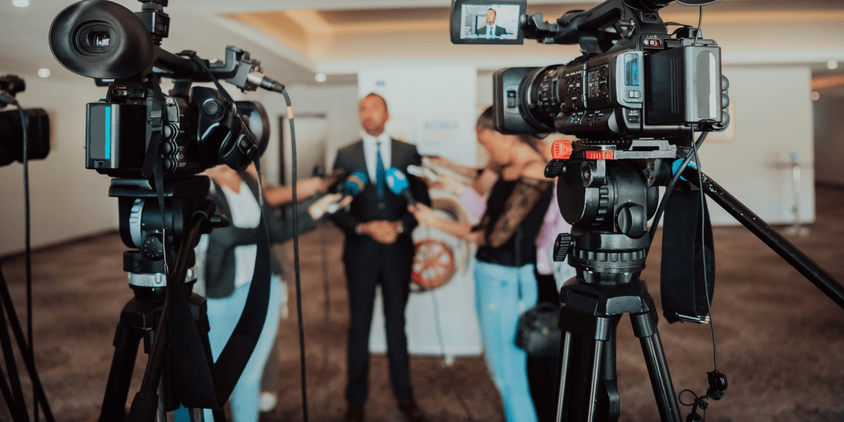 Un dirigeant interviewé par des journalistes avec caméras et micros, illustrant une session de formation média pour des prises de parole publiques et une communication efficace.