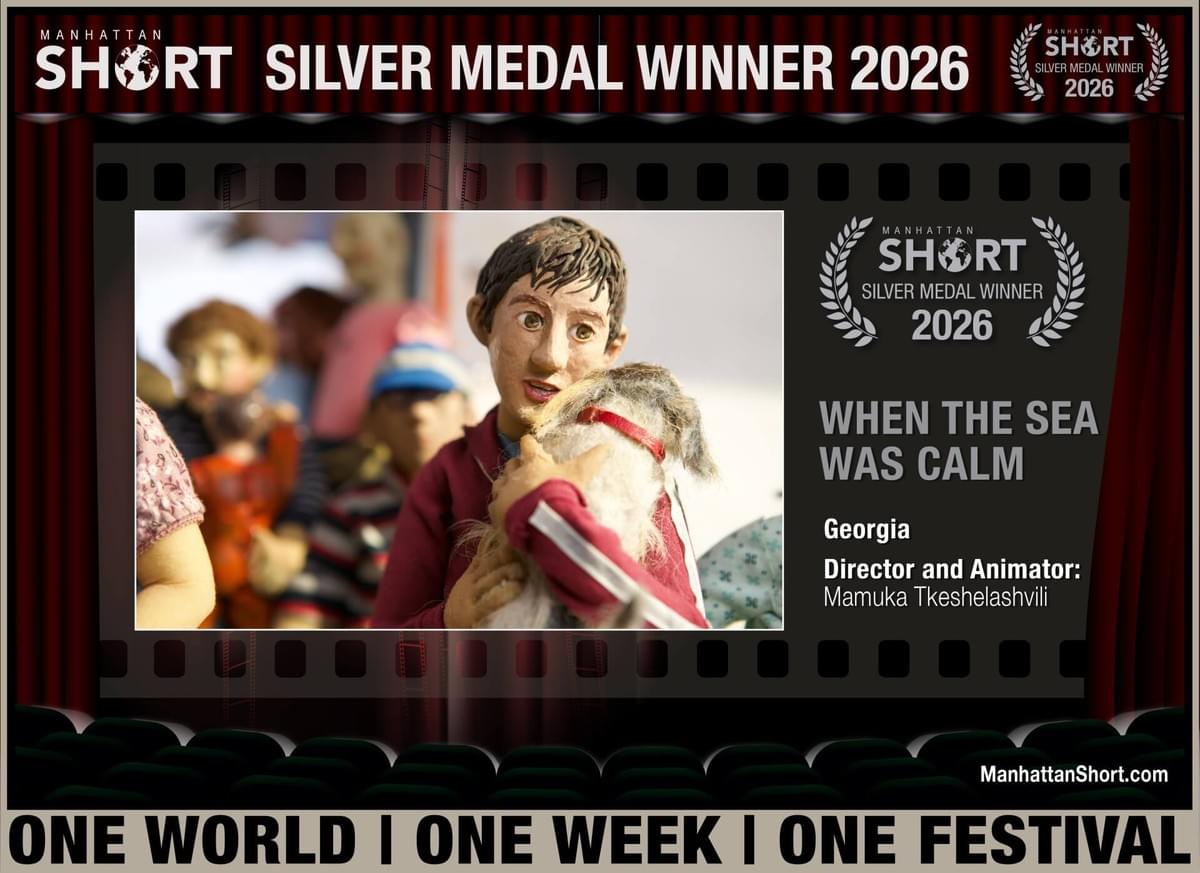 Film festival award poster announces Manhattan Short Silver Medal Winner 2026 for Georgian film “When Sea Was Calm.” Central still shows puppet-like boy holding a small dog, surrounded by filmstrip borders, red curtains, laurel emblem, director-animator Mamuka Tkeshelashvili credit, and “One World | One Week | One Festival” slogan. Film festival award poster announces Manhattan Short Silver Medal Winner 2026 for Georgian film “When Sea Was Calm.” Central still shows puppet-like boy holding a small dog, surrounded by filmstrip borders, red curtains, laurel emblem, director-animator Mamuka Tkeshelashvili credit, and “One World | One Week | One Festival” slogan.