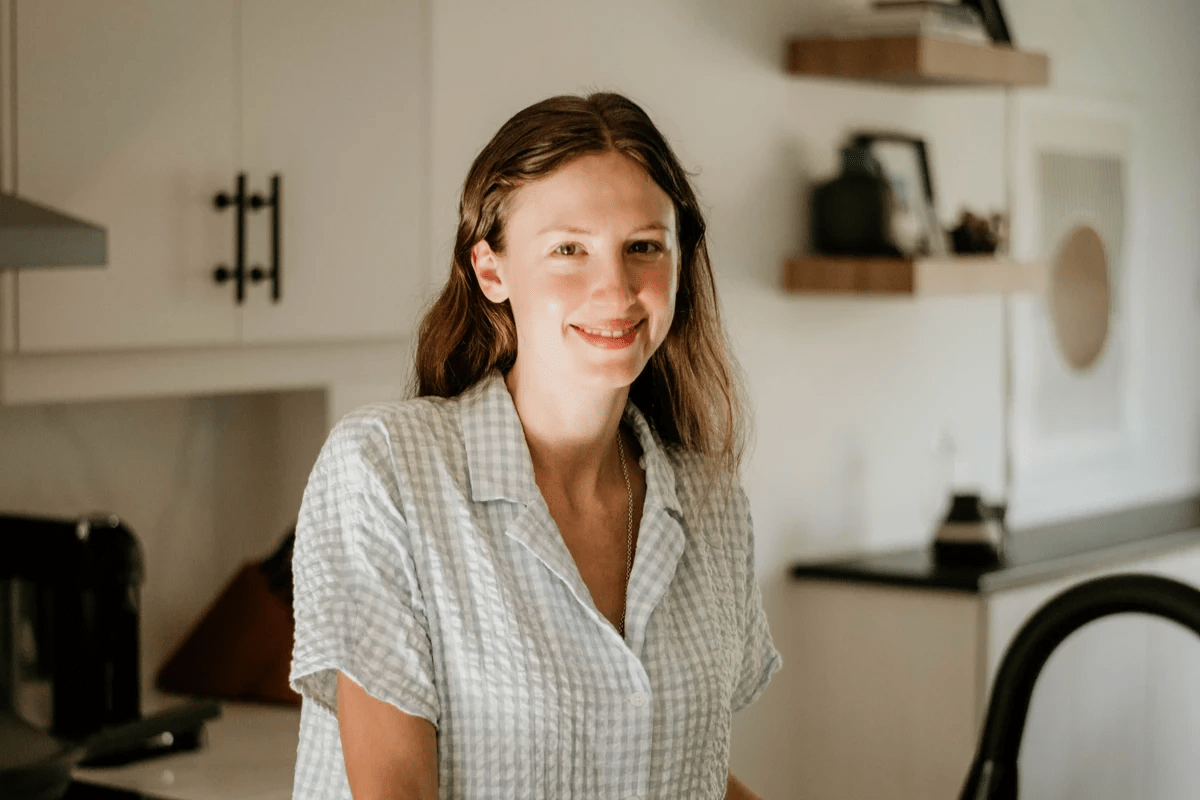 A photo of Aleksa in a kitchen, smiling, with a blue and white gingham dress.