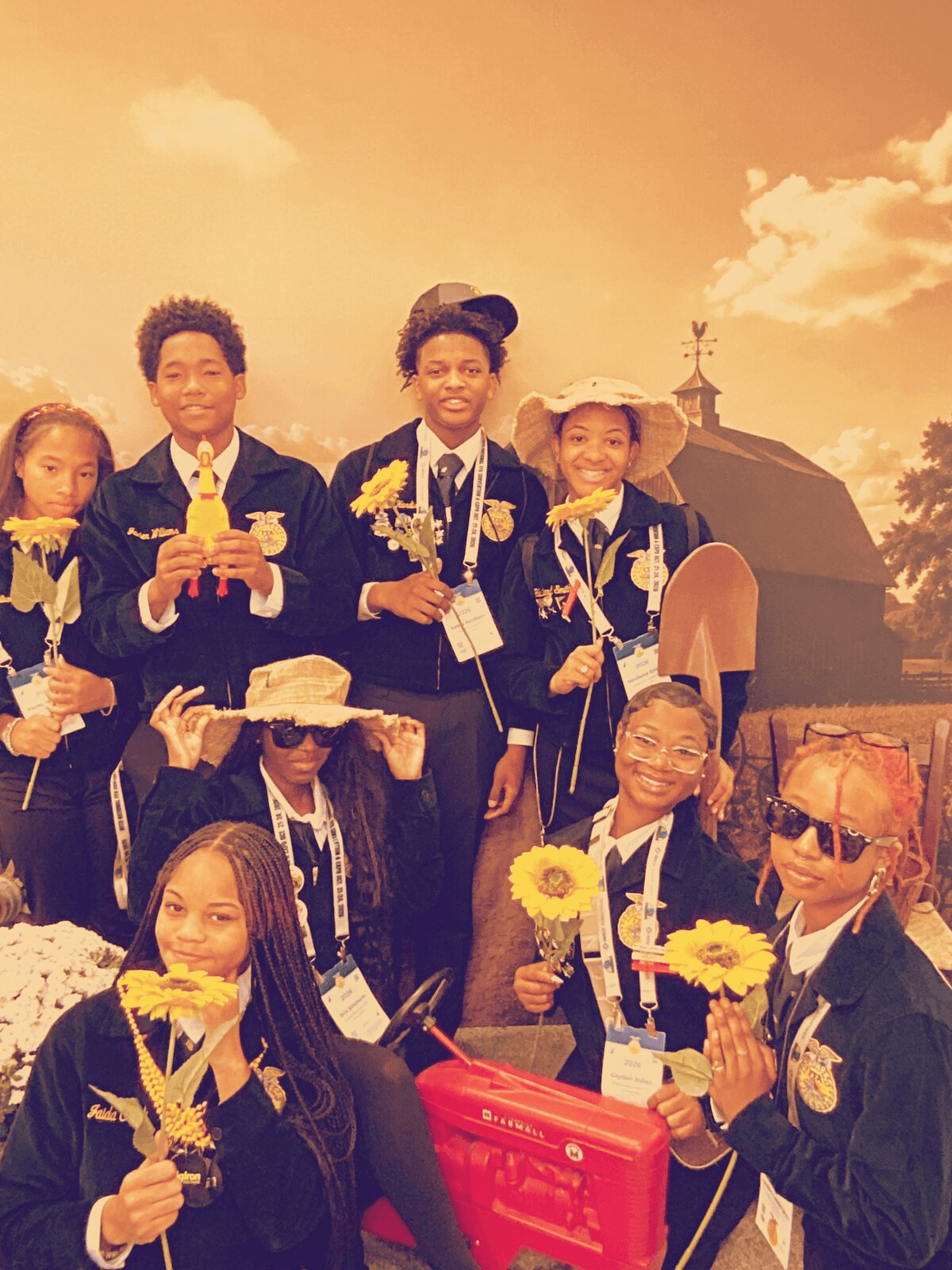 Large group in matching jackets holds sunflowers and wears sunglasses at a farm-themed photo booth