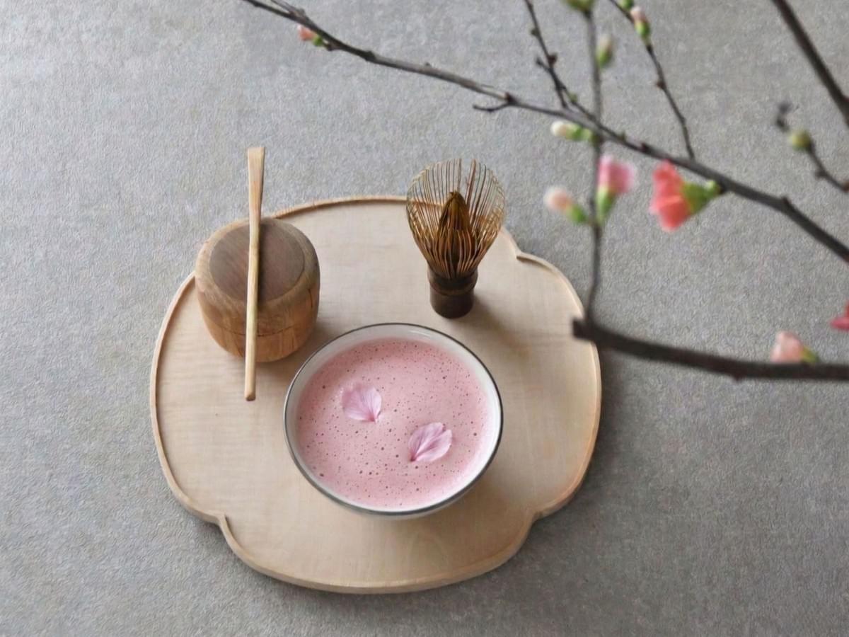 Pink sakura matcha with cherry blossom petals in a Japanese tea ritual setting with matcha whisk and tea tools