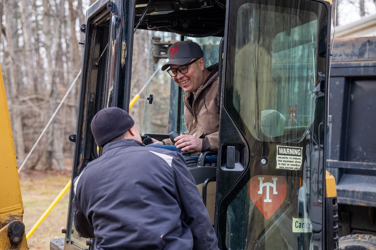 John is laughing from the driver's seat of his bucket loader with the team.