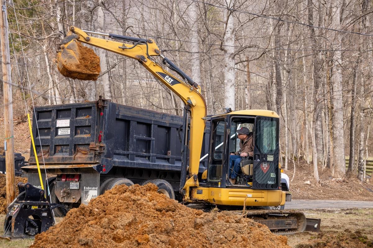 Crane dumping excavation dirt into a dump truck.