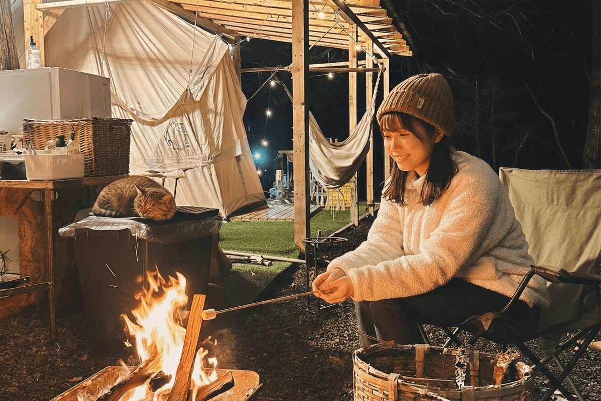 和心村の客室プライベートスペースで焚き火を楽しむ女性と寄り添う猫