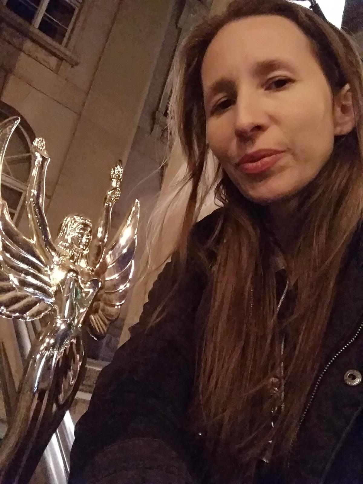 Zdjęcie przedstawiające Iwonę Janicką - uśmiechnięta kobieta w długich włosach, statuetka po lewej