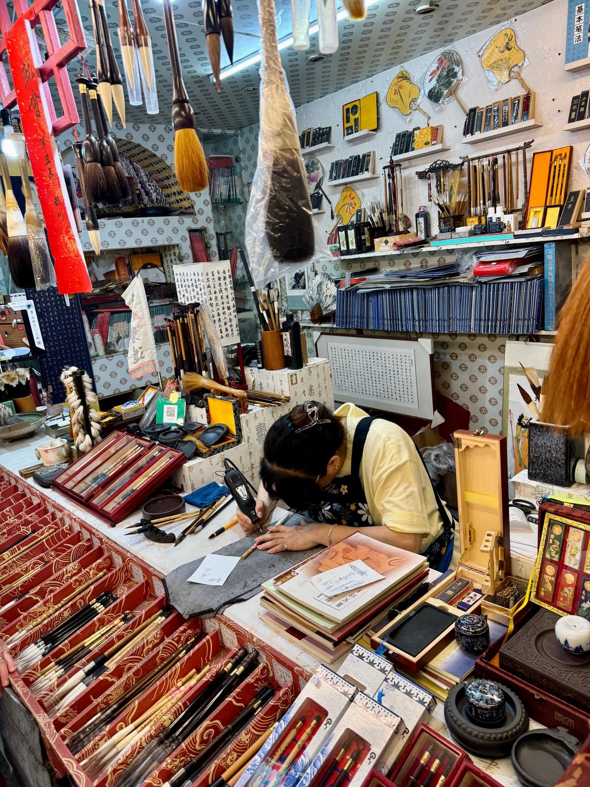 Women carving a name into the handle of a board hair paint brush in Jiufen Od Street