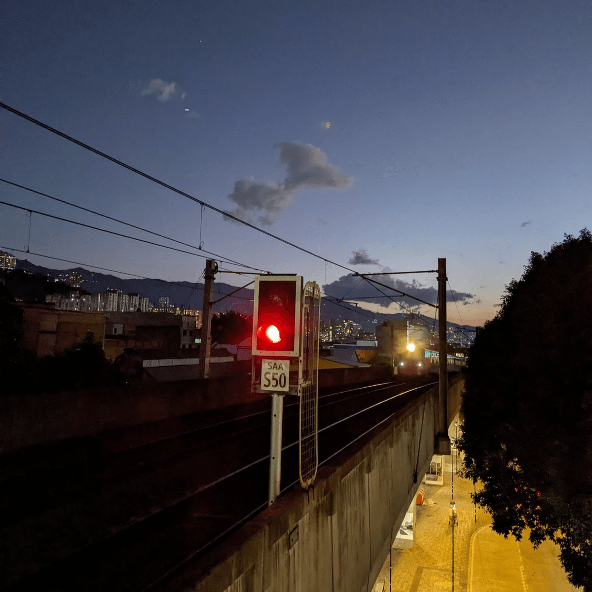 Medellín Metro train arriving at a station with the sun setting in the background