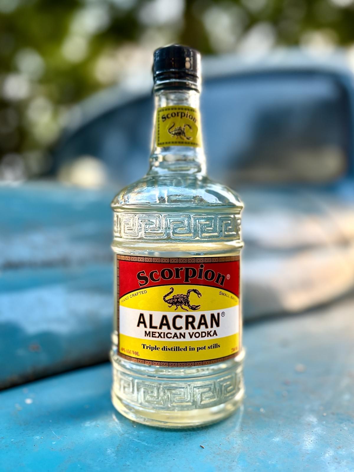 750mL bottle of ALACRAN Mexican Vodka, atop the hood of a turquoise 1940s truck.