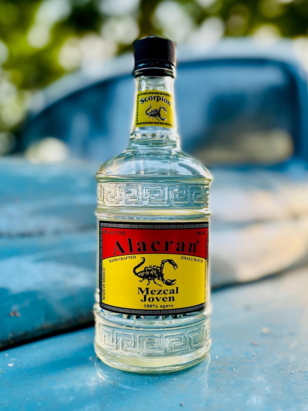 750mL bottle of ALACRAN Mezcal Joven, atop the hood of a turquoise 1940s truck.