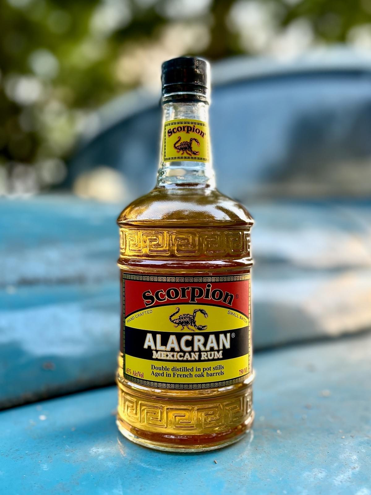 750mL bottle of ALACRAN Mexican Rum, atop the hood of a turquoise 1940s truck.