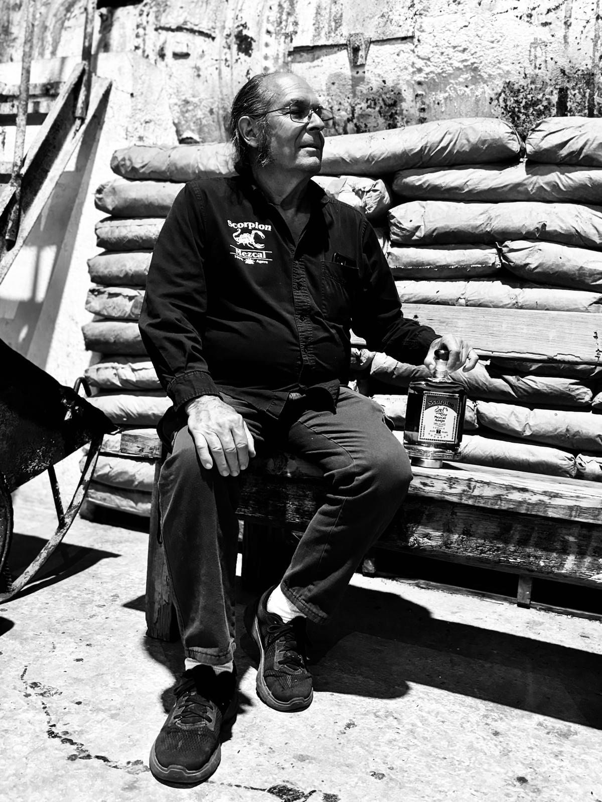 Master Distiller Douglas French seated on a wooden bench holding a bottle of Scorpion Mezcal. 