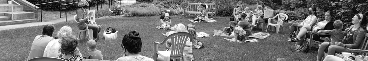 Photo of people of all ages sitting in a circle listening to a teacher share stories.