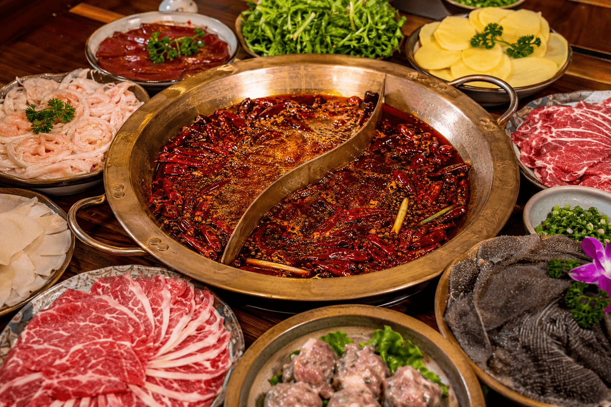 Spicy Chongqing hot pot with red chili broth and fresh ingredients on a restaurant table
