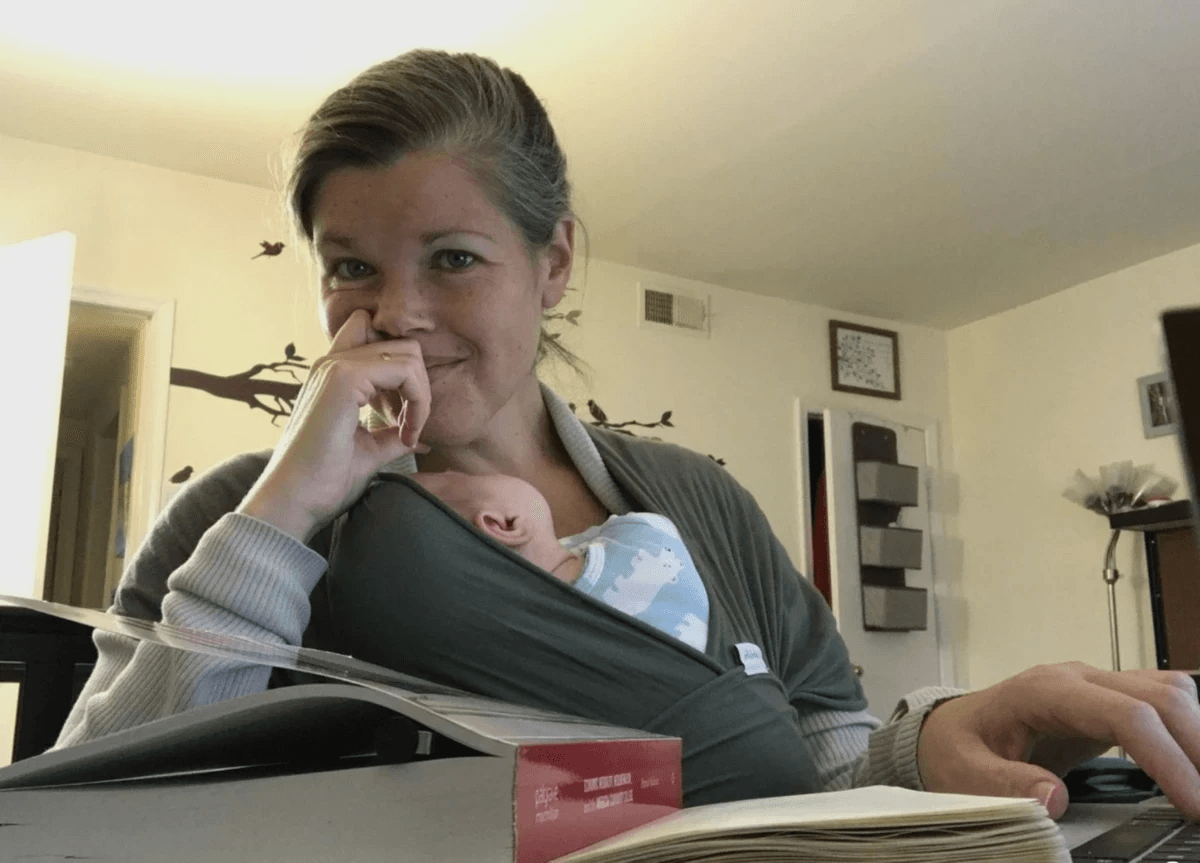 Robyn holding a baby while typing with books open
