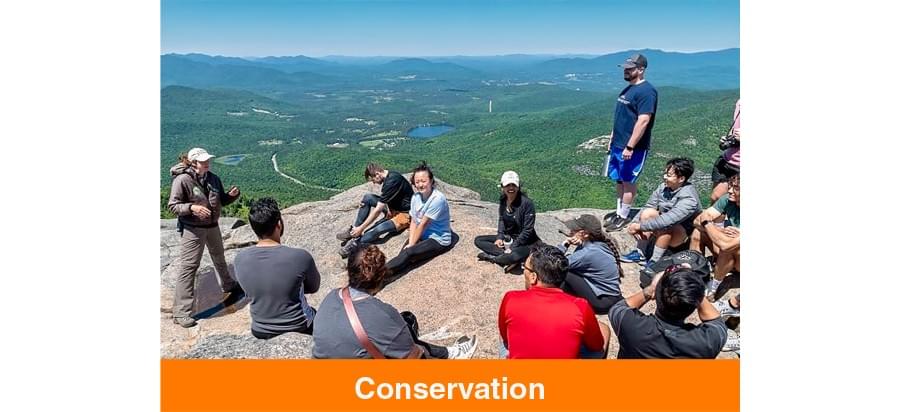 Conservation - Photo of a team of people sitting on a rock formation discussing conservation.