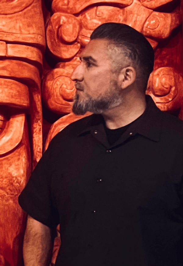 Portrait of Latino sculptor David Morales standing in front of red Aztec-inspired relief sculpture