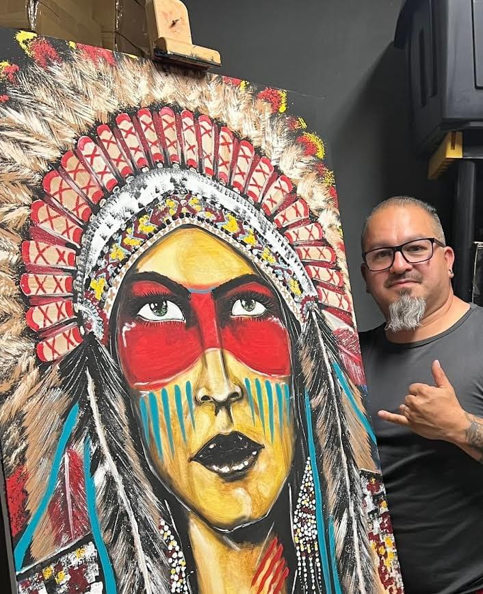 Artist Jose Mares posing next to a vibrant mixed media painting inspired by Mexican culture and traditional headdress design
