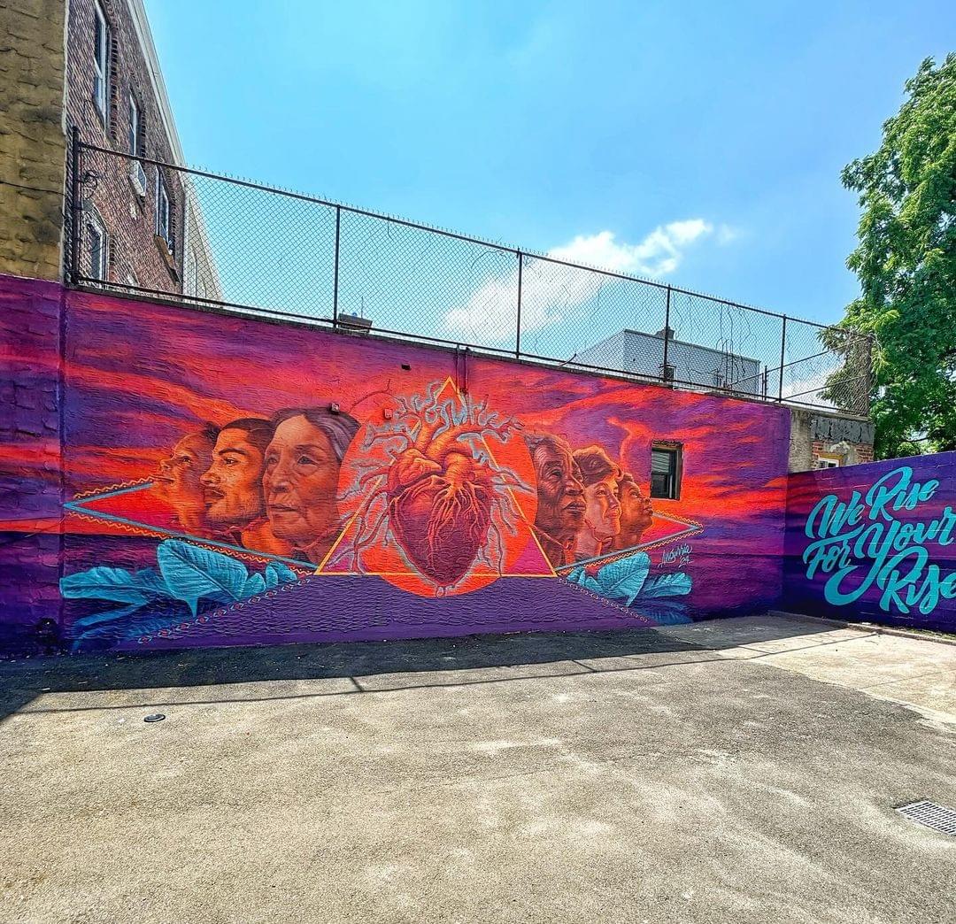 Rising Tide Capital 2024 mural by Angurria featuring community portraits and a central heart symbol in vibrant colors on an outdoor wall