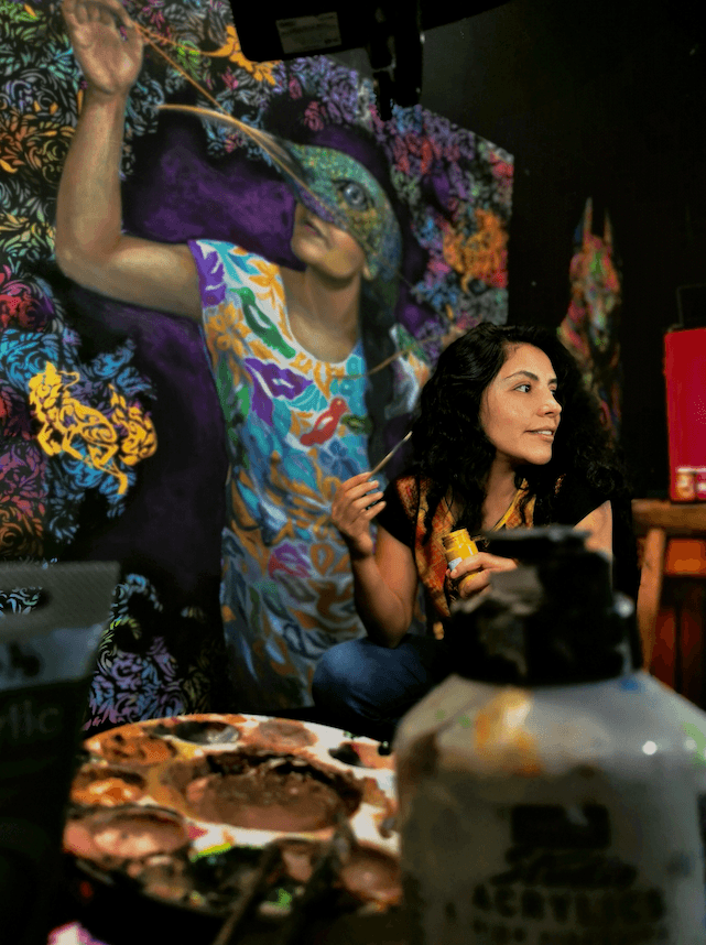 Artist Yuma Diaz painting a colorful mural surrounded by vibrant patterns and symbolic imagery in her creative studio space