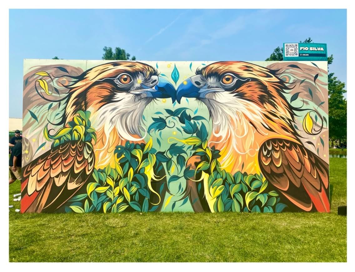 Symmetrical mural by Fio Silva featuring two detailed birds facing each other surrounded by organic plant forms in a vibrant outdoor sett