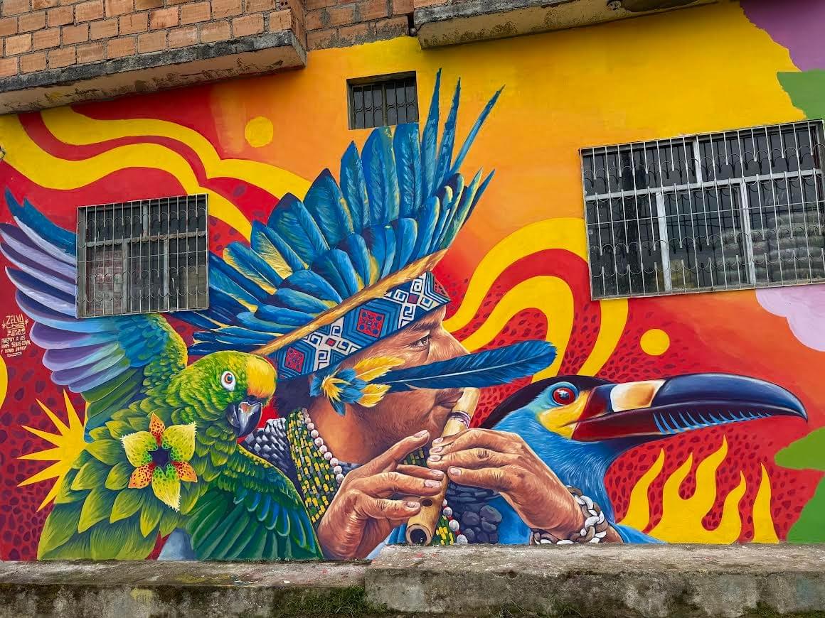 Colorful mural by Zelva Uno of an indigenous musician playing a flute surrounded by a parrot and toucan representing Amazonian culture and nature