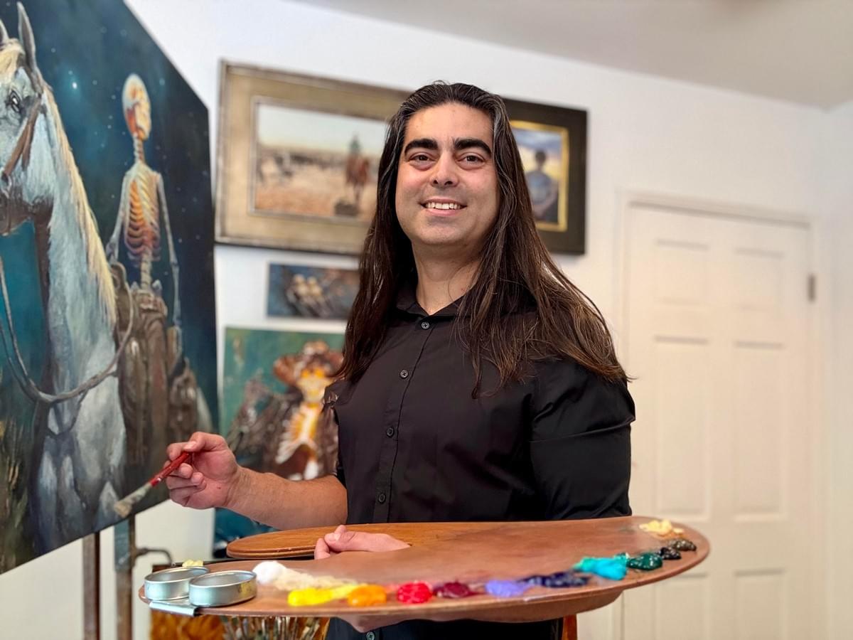 Artist Daniel Gonzalez holding paint palette in studio beside his oil paintings