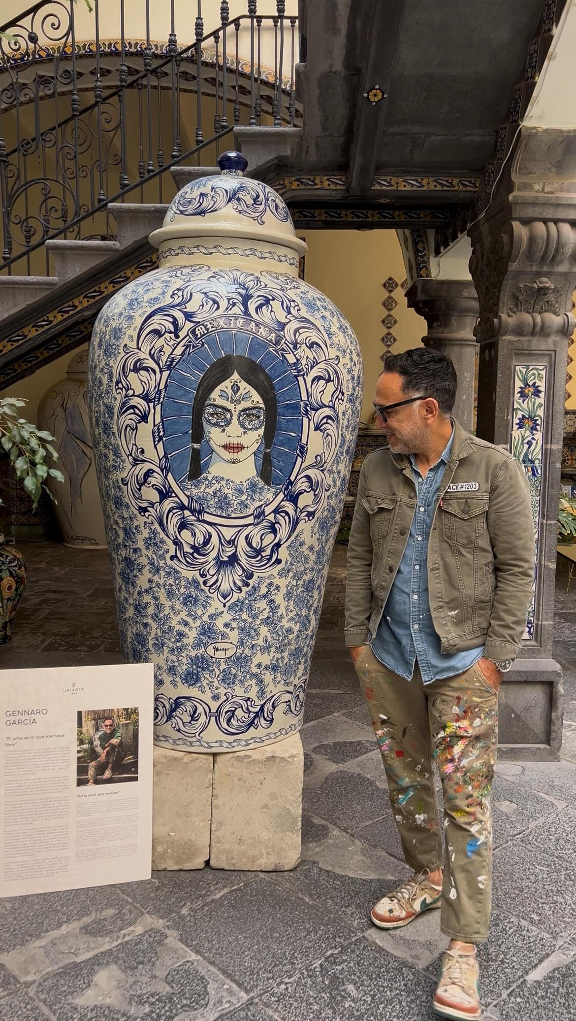 Artist Gennaro Garcia standing beside a large blue and white ceramic vase featuring Day of the Dead inspired Mexican artwork and traditional decorative patterns inside a historic courtyard setting