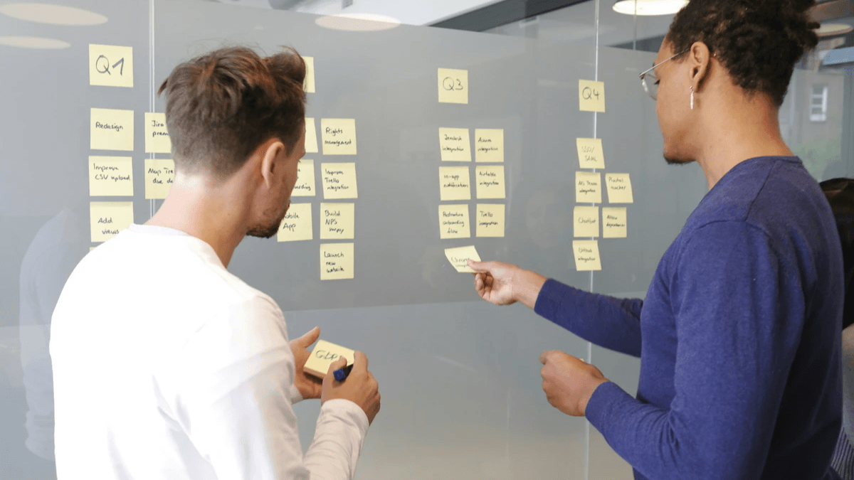 Two people arranging a project roadmap with sticky notes on a glass wall
