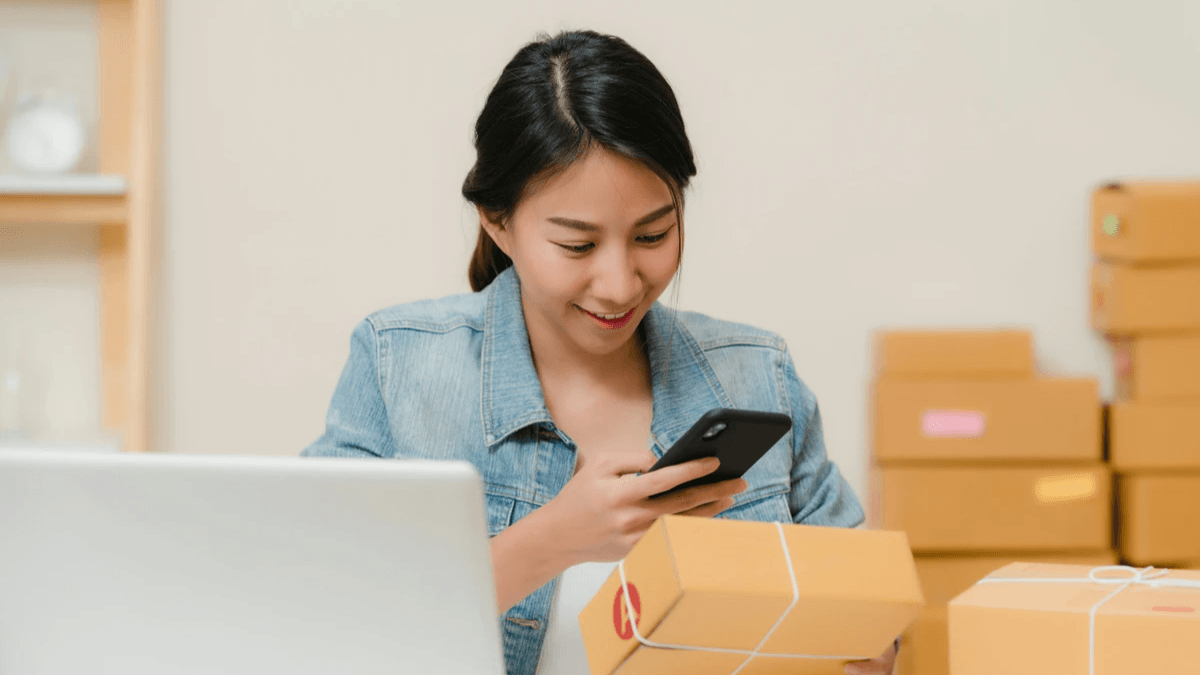 Customer checking a delivered package with a phone beside a laptop