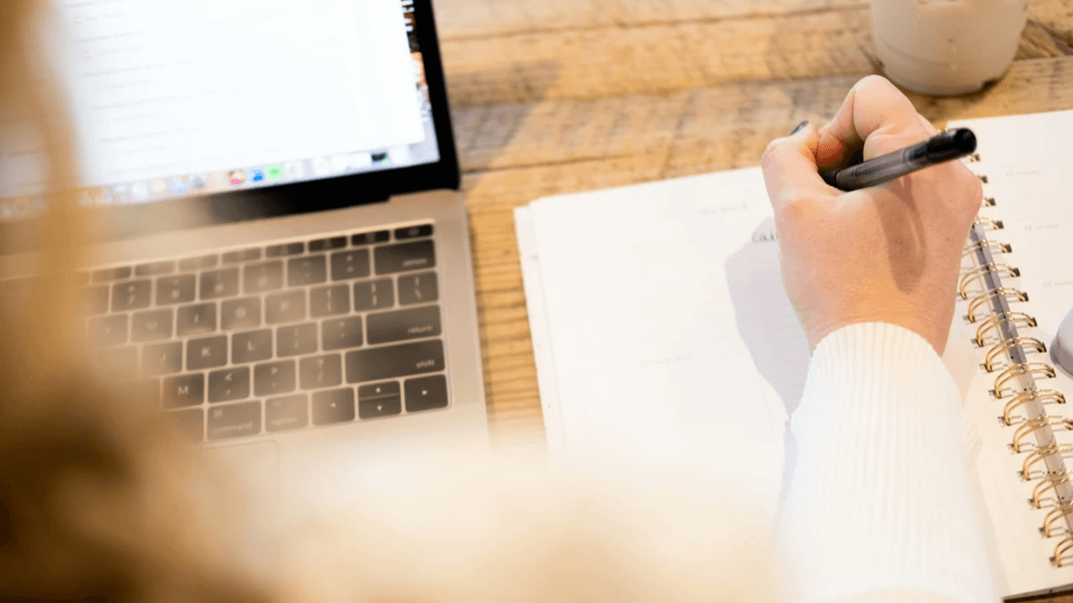 Content writer taking notes beside an open laptop