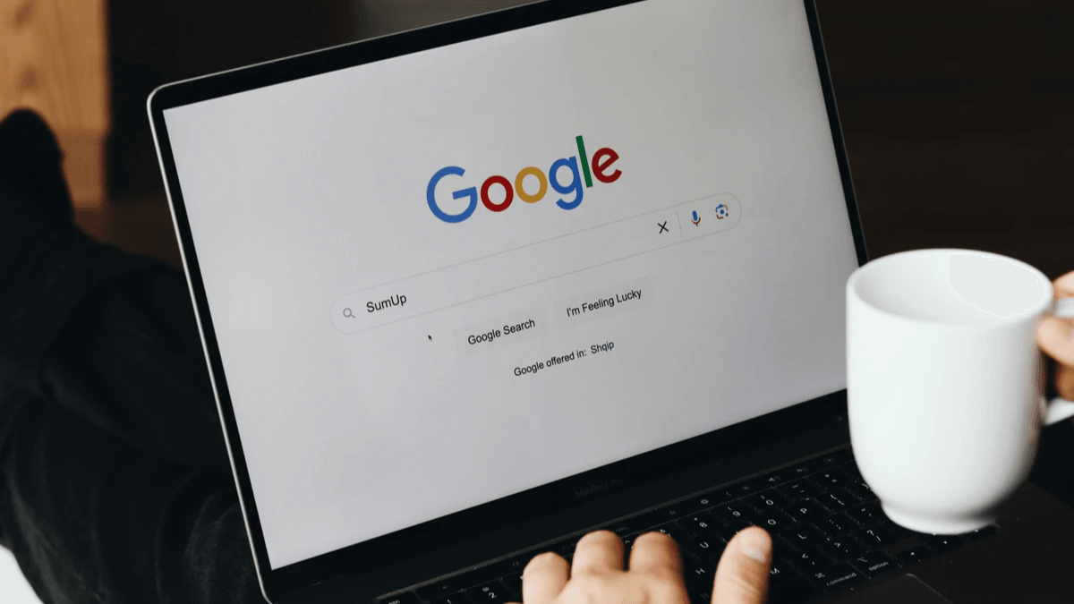 Person using a laptop search page while holding a coffee mug