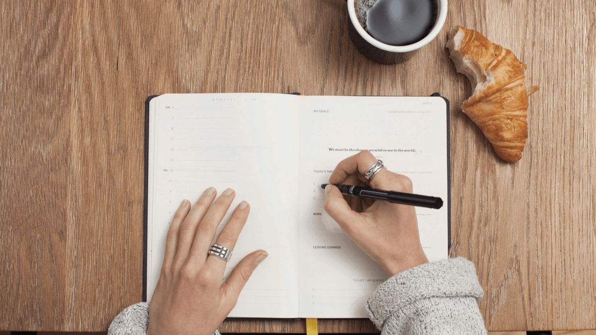 A content creator researching on a laptop while writing ideas in a notebook