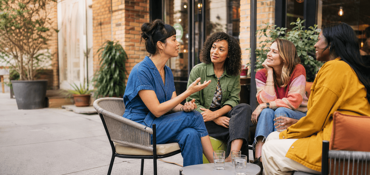 Four diverse women seated together in a lively, thoughtful conversation at a neighborhood café.