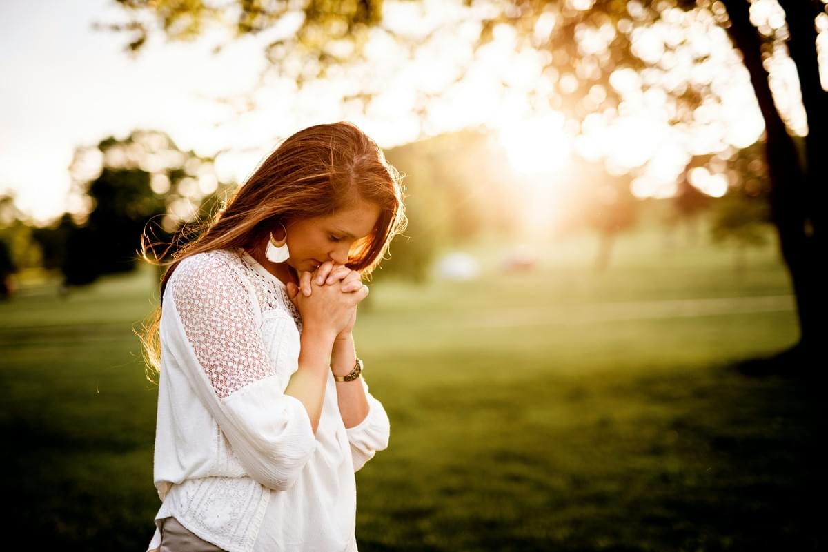 Woman wearing white blouse walking by tree with clasped hands. 